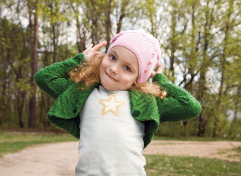 Portrait of the beautiful smiling little girl with long hair in a pink cap in forest
