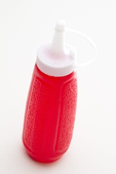 red ketchup bottle with cap close standing upright against a white background