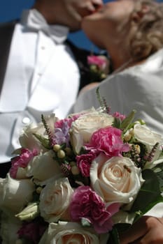 Brid and groom is kissing. The bouquet is in focus.