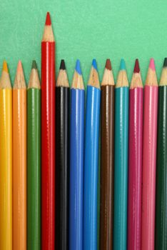 A row of pencil crayons with a red one standing out from the crowd.