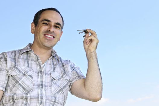 Smiling man holding house keys on blue sky background