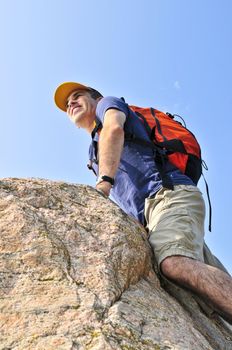 Middle aged man with backpack climbing a rock