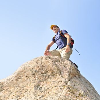 Middle aged man with backpack climbing a rock