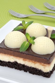 Fanciful chocolate golf cake with mint leaves on a green mat with forks