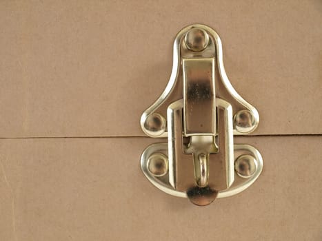 Isolated view of a brass latch on a beige colored container.