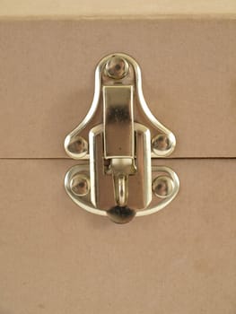 Isolated view of a brass latch on a beige colored container.