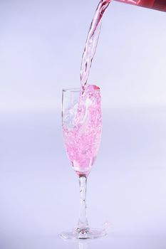 Pink drink bring poured into champagne glass, against blue background