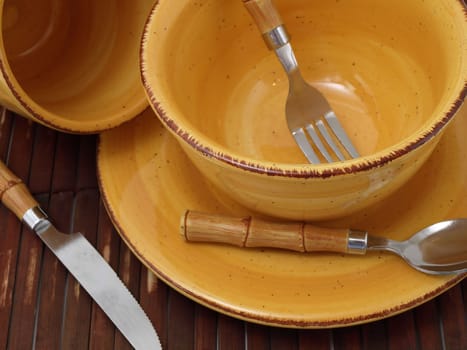 A ceramic bowl on a plate with a cup and utensils in thick earth tones atop a brown bamboo placemat.