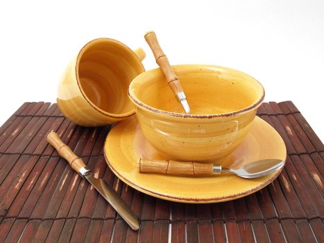 A ceramic bowl on a plate with a cup and utensils in thick earth tones atop a brown bamboo placemat.