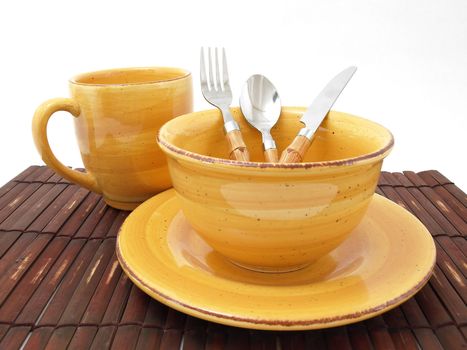 A ceramic bowl on a plate with a cup and utensils in thick earth tones atop a brown bamboo placemat.