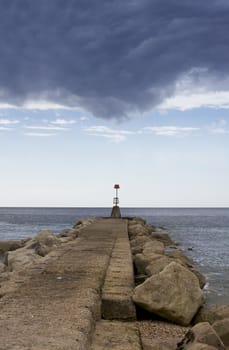 A portrait format image of a groyne marker with a view across the horizon with impending storm clouds above. Located in Christchurch, Dorset, England.