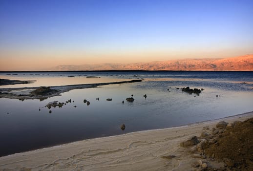 The water of the dead sea with the Jordan mountains and salt sculptures at sunset