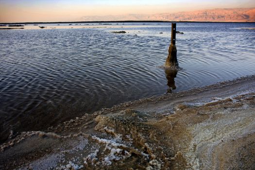 The water of the dead sea with the Jordan mountains and salty sculptures at sunset