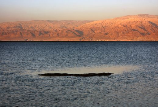The water of the dead sea with the Jordan mountains and salty island at sunset