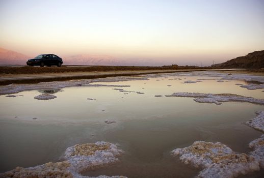 The water of the dead sea with the Jordan mountains at sunset and a car 