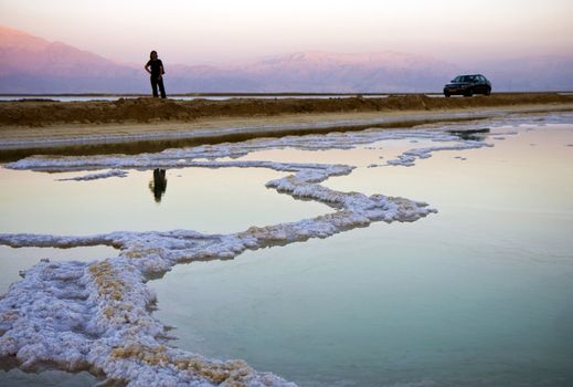 The water of the dead sea with salty paths at sunset and a person and a car