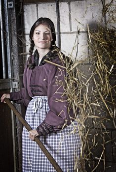 Pretty young girl working in the stable tossing the hay