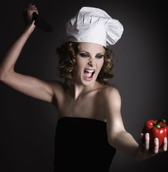 Beautiful girl  with chef's hat and a scream pointing her knife at a pepper
