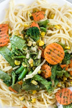 White plate with spaghetti and cooked vegetables.