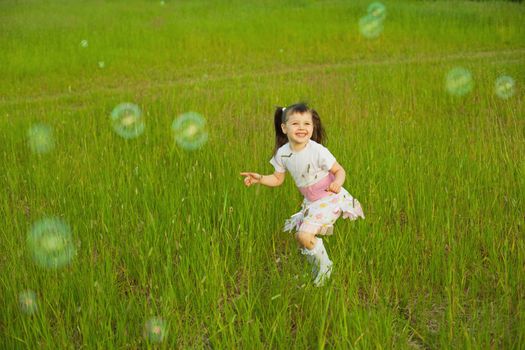 The happy little girl among soap bubbles on field