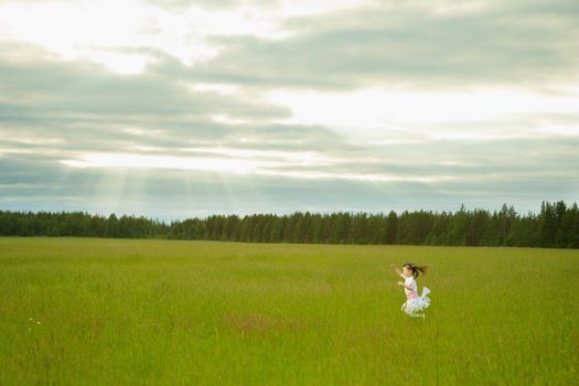 The little girl in a dress runs on a meadow