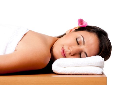 Beautiful happy peaceful sleeping woman at a spa, laying on wooden massage table with head on pillow wearing a towel and pink Calla Lilly flower in hair, isolated.