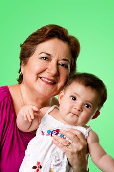 Beautiful happy senior Caucasian Hispanic Latina grandmother holding cute baby in arms, on a green background.
