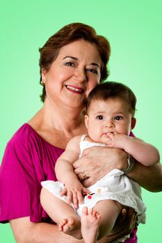 Beautiful happy senior Caucasian Hispanic Latina grandmother holding cute baby in arms, on a green background.