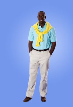 Handsome happy African American corporate business man smiling, standing with hands in pocket, wearing blue shirt and yellow sweater around his neck and khakis, isolated.