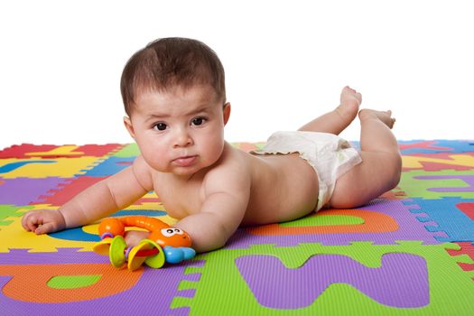 Beautiful cute happy Caucasian Hispanic baby laying on belly on a colorful padded floor tiles with alphabet letters and a toy, isolated.
