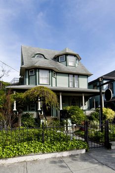 Beautiful green wooden Victorian style building with porch under a blue summer spring sky.