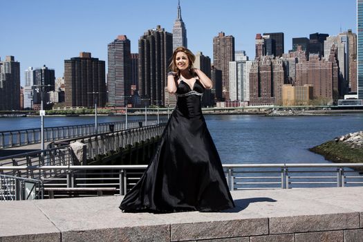 Beautiful happy Caucasian Latina fashion model woman in black evening cocktail dress posing standing in front of skyline of Manhattan, New York City.