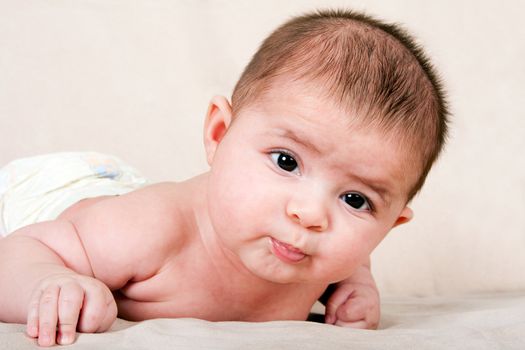 Cute Caucasian Hispanic baby infant laying on belly lifting head making funny expression.