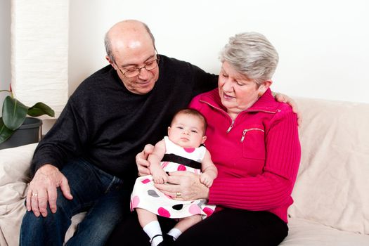 Grandparents holding baby girl on lap while sitting on couch in livingroom as a happy family.