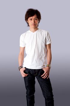 Casual Asian man wearing white shirt and jeans standing with thumbs in pockets, isolated.