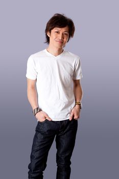 Smiling casual Asian man wearing white shirt and jeans standing with hands in pockets and happy expression, isolated.