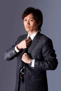 Successful Asian business man standing with confidence and fixing his necktie, isolated.