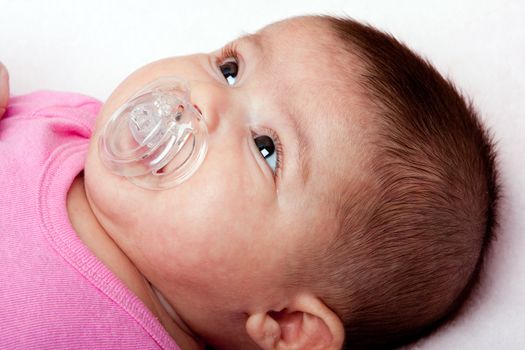Beautiful Caucasian hispanic latina baby infant girl with plastic pacifier. Cute face of a newborn.