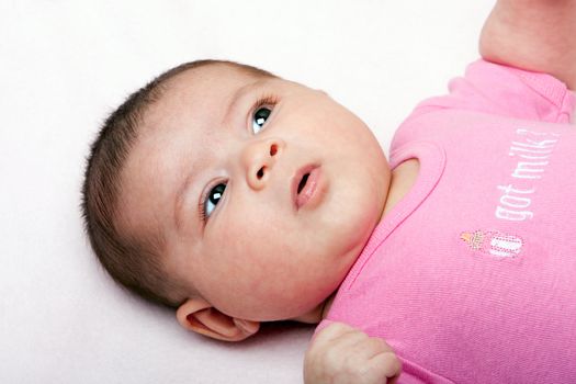 Cute Caucasian Hispanic infant baby face with funny expression wearing pink.