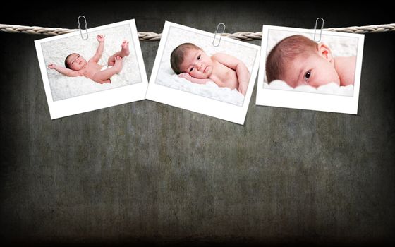 Three funny cute Caucasian Hispanic baby photos with white frame hanging on rope with paperclips on a gray grunge background.