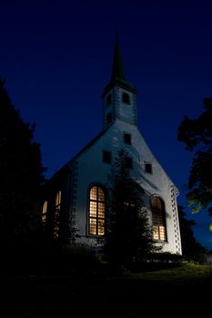Night view of small white church with illuminated windows.