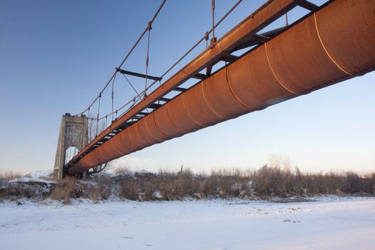 rusty abandoned flume of irrigation ditch suspended over a river in Colorado farmland, winter scenery