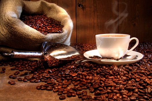 Coffee cup with burlap sack of roasted beans on rustic table