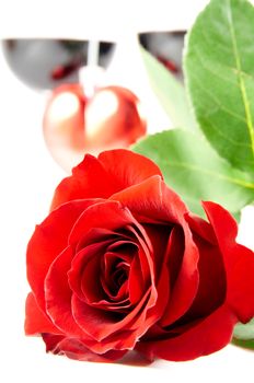 Close-up of red rose with heart and two glasses with red wine on background