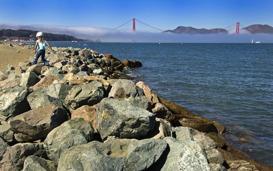Morning Mist covers the Golden Gate Bridge as a little girl plays in the rocks.