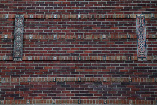 Large red brick wall with sectons of designed tiles