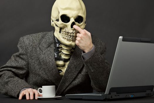 The skeleton picks in a nose on table with laptop