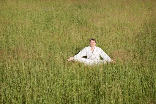 The man in a kimono meditates sitting in a grass