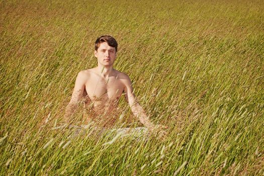 The man sits in a grass in a lotus pose