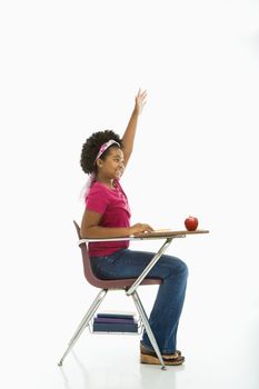 Side view of African American girl sitting in school desk raising hand.